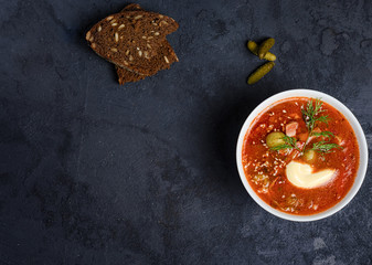 Tomato soup with meat, olives, herbs in white bowl, black bread. Solyanka