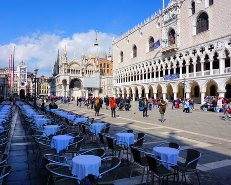 Venice, Veneto / Italy - March 2018: Tables sit mostly empty while tourists mill around St Mark's Square near Doge's Palace in Venice, Italy.