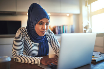 Young Arabic woman working on a laptop in her kitchen