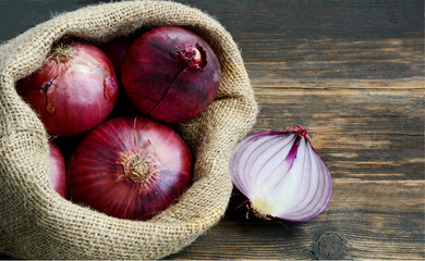 Red onions in sack bag on wooden floor.  A Red onions are good to eat raw, chopped or sliced into salads, salsas, dressings and marinades © posinote