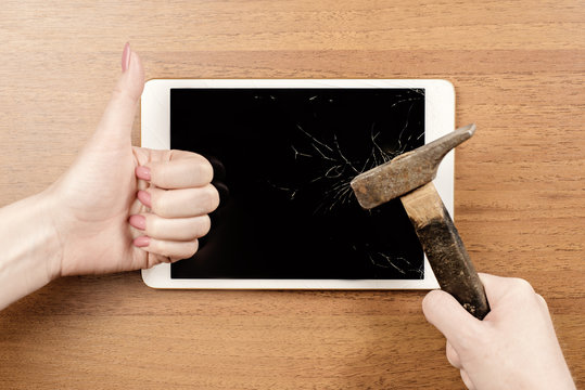 Conceptual photo of broken tablet with thumb up finger and a hummer. Top view on the wooden table
