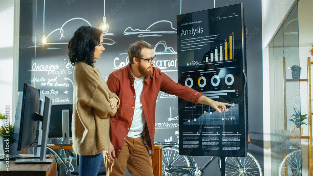 Poster Female Developer and Male Statistician Use Interactive Whiteboard Presentation Screen to Look at Charts, Graphs and Growth Statistics. They Work in the Stylish Creative Office.