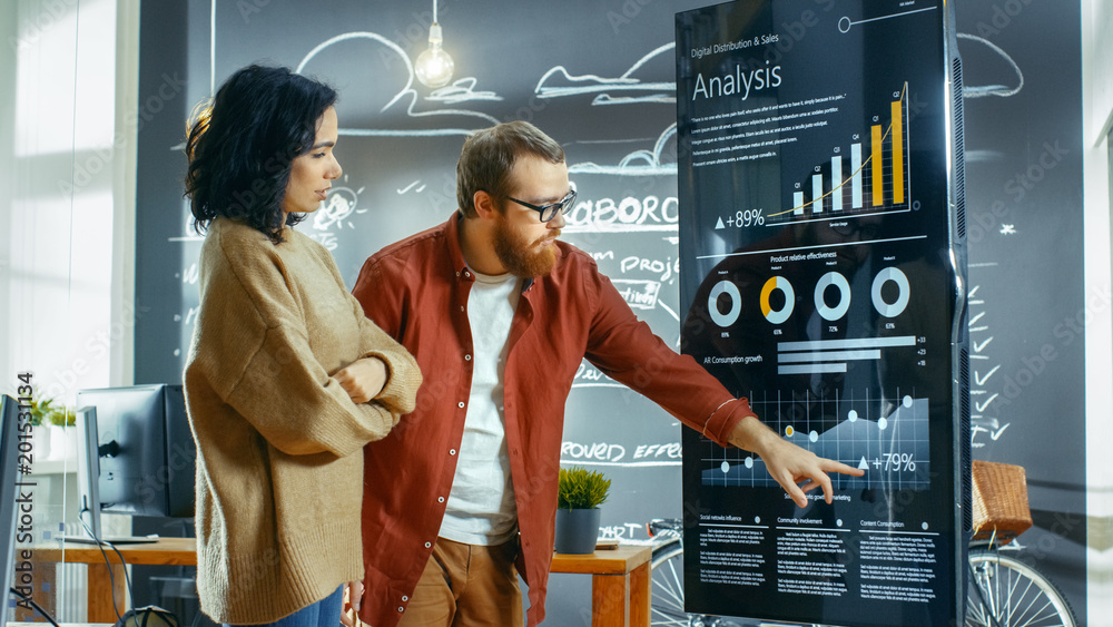 Poster Female Developer and Male Statistician Use Interactive Whiteboard Presentation Touchscreen to Look at Charts, Graphs and Growth Statistics. They Work in the Stylish Creative Office.