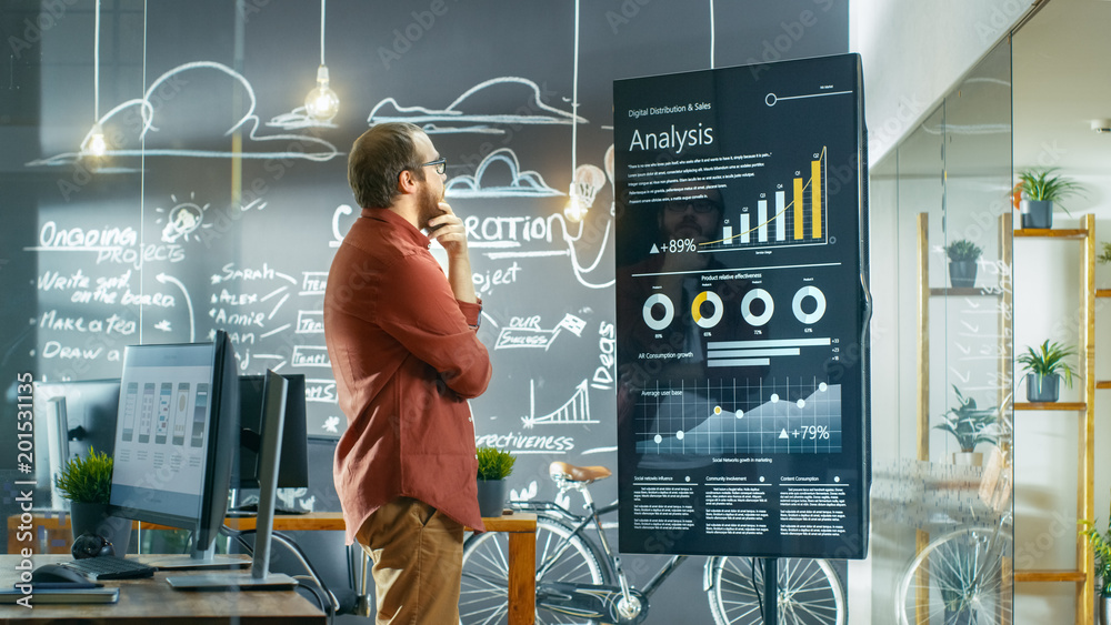 Poster Marketer Looks at Interactive Touchscreen Whiteboard Showing Latest Graphs and Charts on Statistical Growth. He Works in the Creative Office.