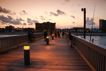 Obraz premium Deerfield Beach, promenada na molo na Florydzie po zmierzchu z oświetlonymi światłami, ławeczki w parku, Ocean Atlantycki po obu stronach i hotel Wyndham w oddali