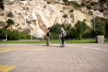 Two guys enjoy a ride on mono wheels on the beautiful park of the Rock of Ifach on the Mediterranean coast of Spain © Olga