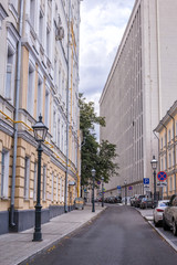 Узкий Староваганьковский переулок в центре Москвы, Россия. Высокие здания разных архитектурных стилей почти полностью закрывают небо