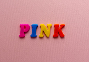 word 'pink' from plastic colored magnet letters on pink paper background
