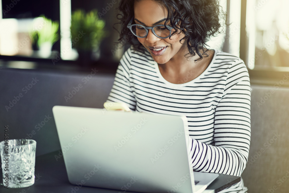 Wall mural Smiling young African woman using a laptop and reading texts