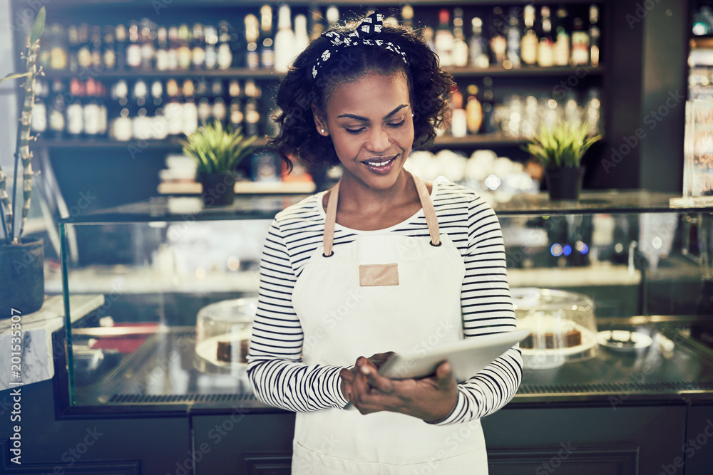 Wall mural smiling african entrepreneur working in her cafe with a tablet