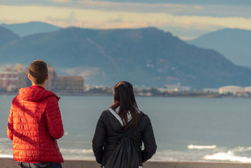 A couple of a boy and a girl on the beach with the mountains in the background and azil sky