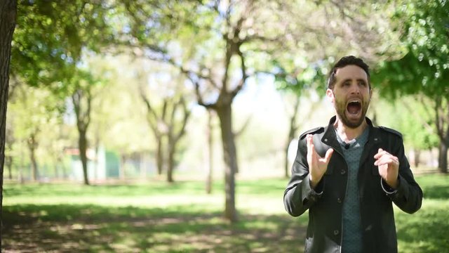 Hombre joven moreno con chaqueta verde bostezando en un parque/bosque