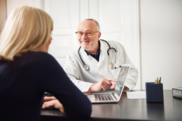 Cheerful adult medical worker showing laptop to patient