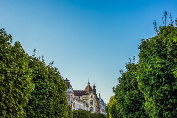 Obraz premium beautiful old city view in green space district with trees on foreground medieval building on background and empty space for copy or text on blue sky 