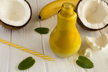 Cocktail with coconut  milk  and banana in the glass yellow lamp  on the white  wooden background