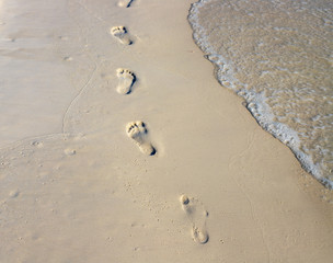 Barefoot walk chain on wet white sand. Beach view photo. Foot marks on beach.