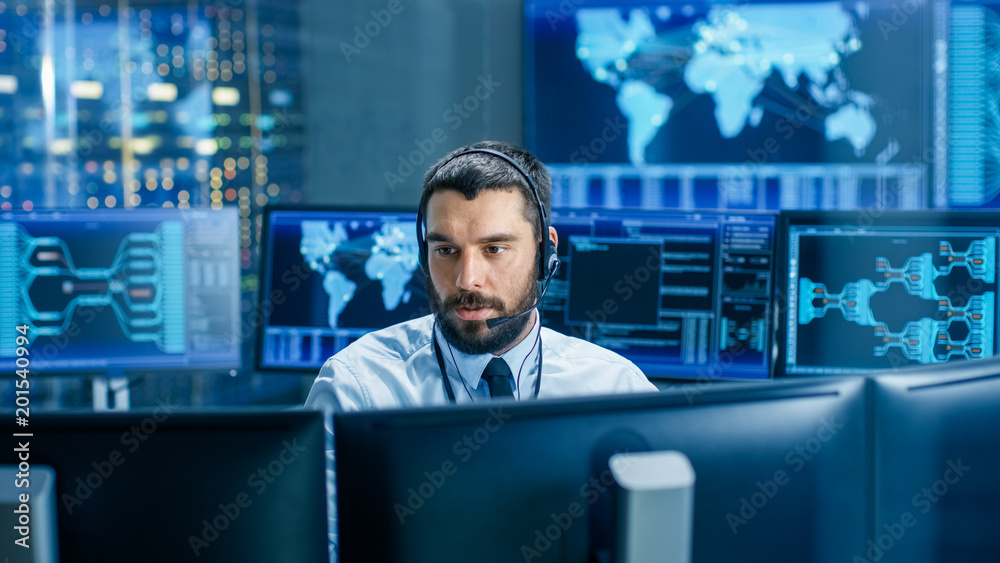 Leinwandbilder In the System Monitoring Room Dispatcher Wearing Headset Observers Proper Functioning of the Facility. He's Surrounded by Screen Showing Technical Data.