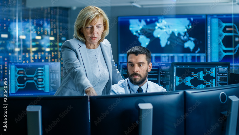 Poster In the System Monitoring Room Senior Supervisor Controls Work of the Operator. They're Surrounded by Monitors Showing Relevant Technical Data.