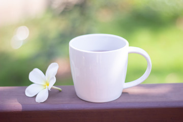 Fototapeta na wymiar Selective focus white coffee mug and flower are placed on wooden floor with blurred background.