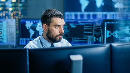 In the Monitoring Room Technical Operator Attentively Monitors Stability of the System. He's Surrounded By Screens Showing Technical Data.