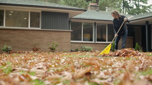 Woman raking leaves in garden, panning left. 