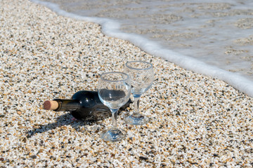 Bottle of red wine with wine glasses on the beach at the summer sunny day.