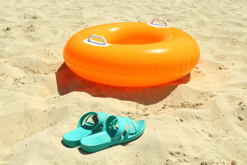 Orange swimming circle and blue female slates on beach sand. Close-up. Background.