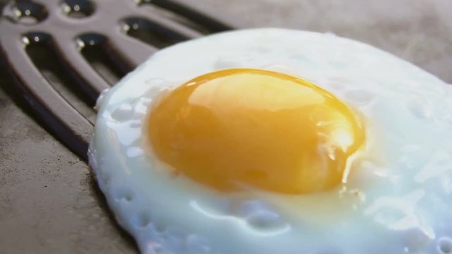 Cook picks up fried egg with a spatula from the stone grill