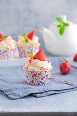 Homemade muffins or cupcakes with vanilla cream and fresh strawberries on the light grey background