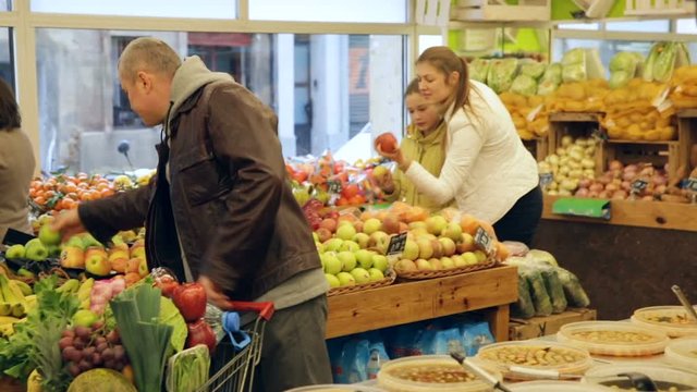 Cheerful family with preteen daughter standing with full grocery cart after shopping in fruit store