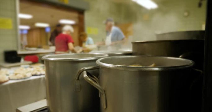 Pots boiling on the stove as cafeteria workers prepare food in the background.  	