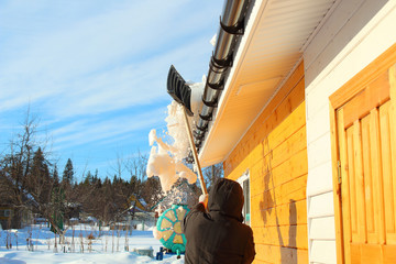 The man takes the snow from the edge of the roof with a shovel. The arrival of spring. Russia,...