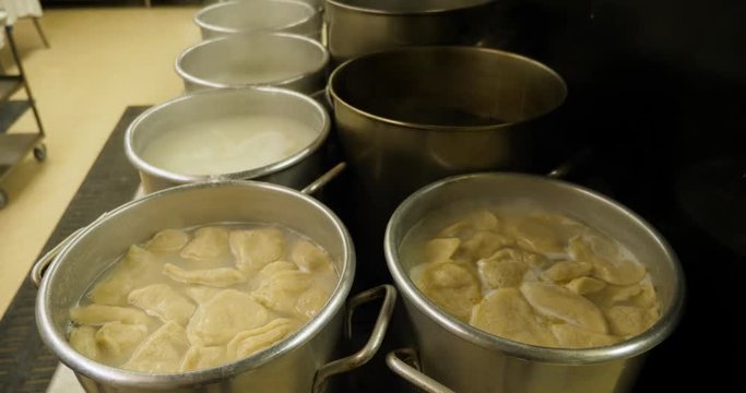 A cafeteria cook stirs pierogies boiling in large pots on an industrial stovetop.  	