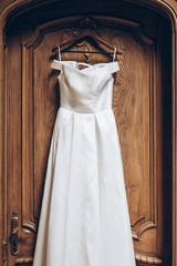 beautiful classic silk dress hanging on old wooden wall in room. morning preparation. gown shopping
