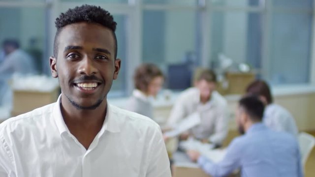 Tilt up of joyous african american businessman using digital tablet and smiling at camera in new office after relocation while his colleagues having meeting in background