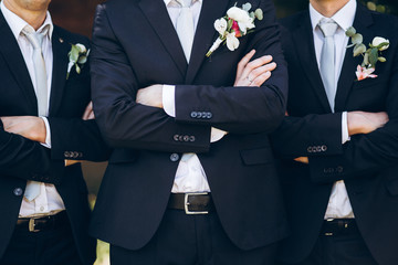 stylish groom in suit posing with groomsmen in garden on wedding day. luxury men in  rich outfits...