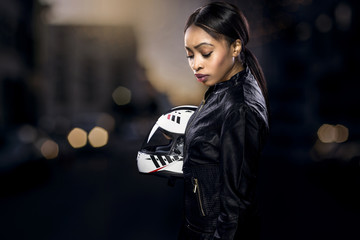 Black female motorcycle rider or race car driver wearing a racing helmet and leather jacket. Part...