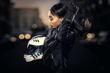 Black female motorcycle rider or race car driver wearing a racing helmet and leather jacket. Part...