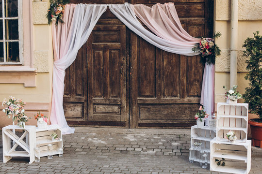 rustic wedding photo zone. wooden barn doors with fabric and white boxes with flowers and candles at stylish wedding photo booth. shabby chic. luxury arrangements