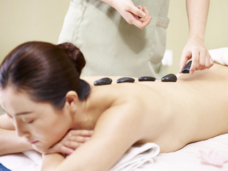 Obraz na płótnie Canvas young asian woman receiving hot stone massage in spa salon