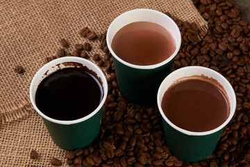 Three green paper coffee cups with coffee beans. Take away coffee cups with hot chocolate drink on wooden background.