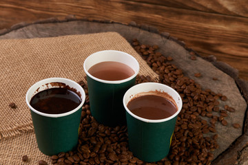 Three green paper coffee cups with coffee beans. Take away coffee cups with hot chocolate drink on wooden background.
