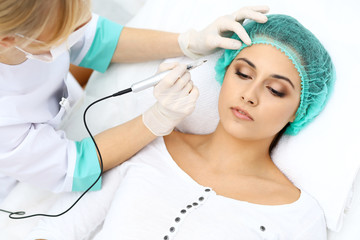 Naklejka premium Professional beautician doing eyebrow tattoo at woman face. Permanent brow makeup in beauty salon, closeup. Cosmetology treatment
