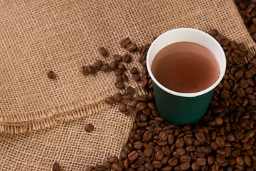 Green Take away coffee cup with roasted coffee beans on wooden background, close-up