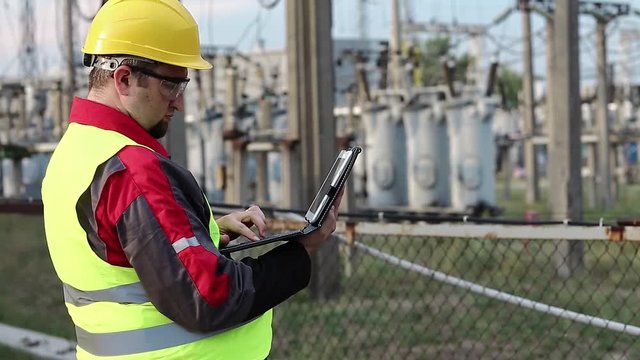 Electrician with computer on power station. Worker in hard hat at electric power plant, engineering supervision. Factory worker with tablet pc