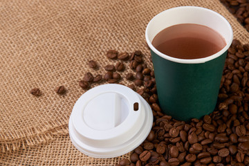 Green Take away coffee cup with roasted coffee beans on wooden background, close-up