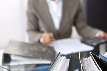 Binders with papers are waiting to be processed with businesswoman or secretary back in blur