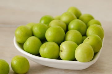 A bowl of fresh green plums on table