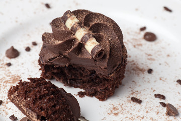 Chocolate cupcake on white plate with fork, dusted with cocoa powder and chocolate sprinkles, half eaten
