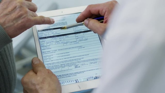 Over the shoulder shot of unrecognizable male doctor showing form on tablet to patient and explaining something